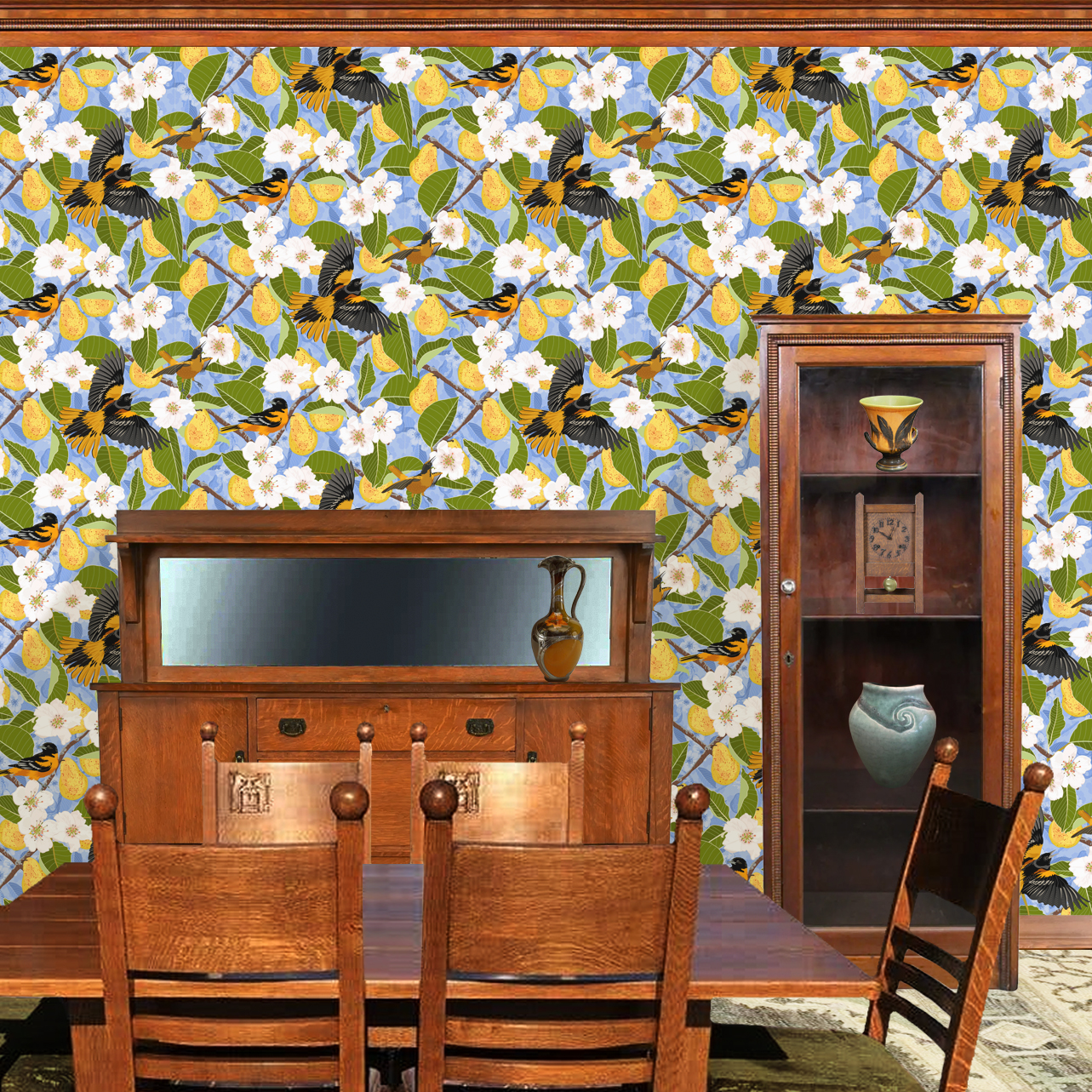 The artwork showcases a vibrant and detailed pattern featuring three orange and black birds set against a backdrop of yellow pears, green leaves, and white blossoms. The birds are depicted in different poses: one perched on a branch, one in mid-flight with wings spread, and another near a pear. The rich colors and intricate details of the feathers, fruits, and flowers create a lively and harmonious composition. The overall style combines naturalistic elements with a decorative, repeating design, highlighting the beauty of nature with emphasis on bold contrasts and vivid hues. The wallpaper design is shown in a Mission style dining room.