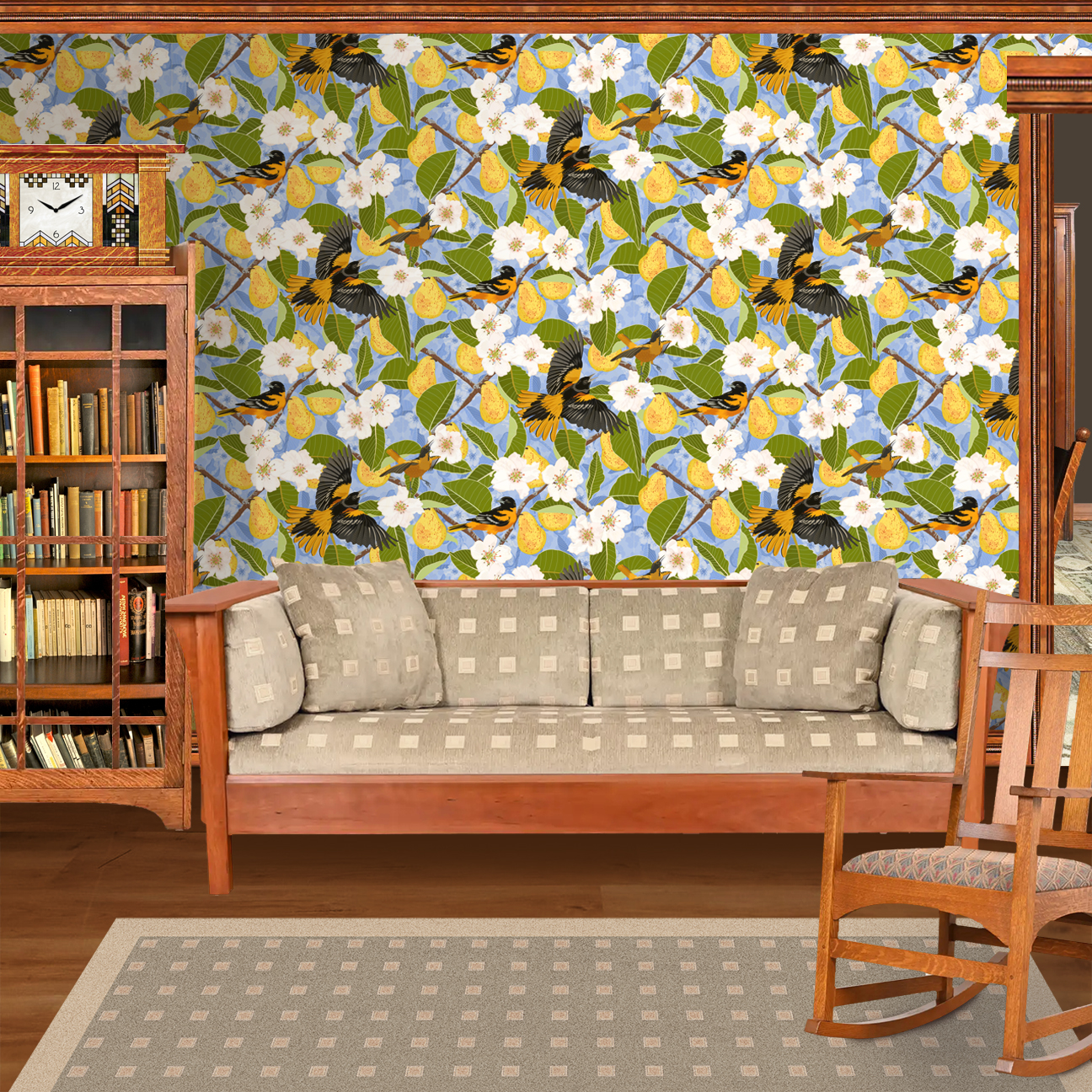 The artwork showcases a vibrant and detailed pattern featuring three orange and black birds set against a backdrop of yellow pears, green leaves, and white blossoms. The birds are depicted in different poses: one perched on a branch, one in mid-flight with wings spread, and another near a pear. The rich colors and intricate details of the feathers, fruits, and flowers create a lively and harmonious composition. The overall style combines naturalistic elements with a decorative, repeating design, highlighting the beauty of nature with emphasis on bold contrasts and vivid hues. The wallpaper design is shown in a Mission style living room