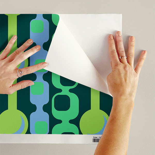 The artwork features a repeating geometric pattern of symmetrical shapes resembling elongated, curved diamonds or petals in various shades of blue and green. Each shape is split vertically with one half filled with a light blue and the other half filled with green or darker blue. The background is a light, almost pastel blue, which provides a soft yet vibrant backdrop. One of the blue shapes near the upper left contains a white starburst element, adding a focal point of brightness to the composition. The overall design conveys a modern, mid-century aesthetic with clean lines and harmonious color contrasts.